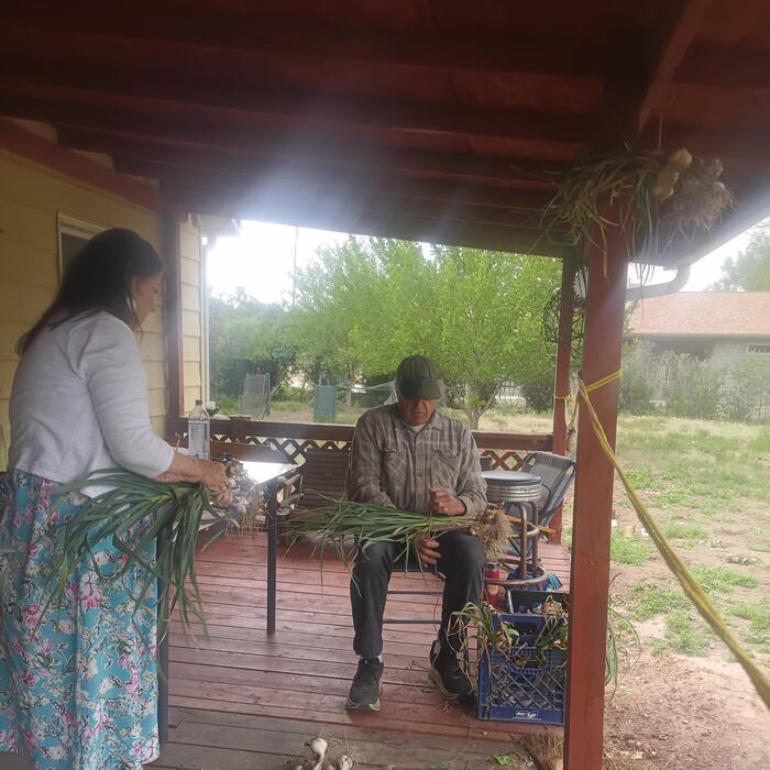Freshly pulled onions being carried up onto the porch, another member seated and trimming.