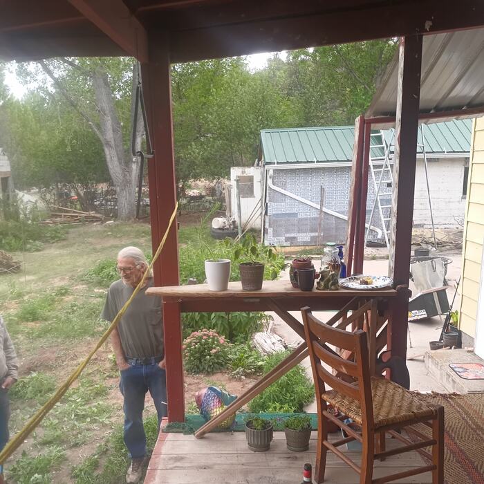 Members gathered on the porch beside potted starts, the garden and outbuildings behind.